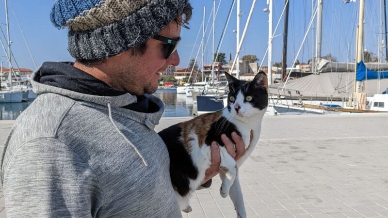 a man carrying a cat through a marina they live in