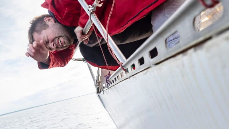 a sailor being seasick off the side of a sailboat