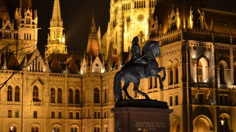a statue of a man rising a horse with the church in budapest lit up behind him