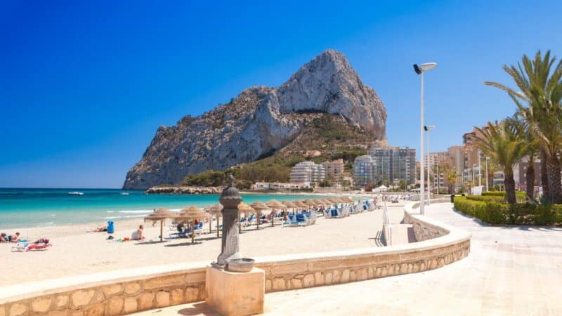 a beach with a huge rock at the best time to visit spain