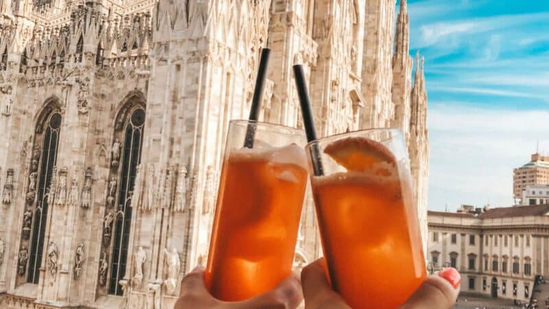 two drinks clinking outside a famous landmark in milan
