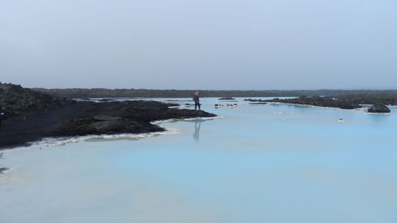 a girl standing on the edge of a blue lagoon in iceland
