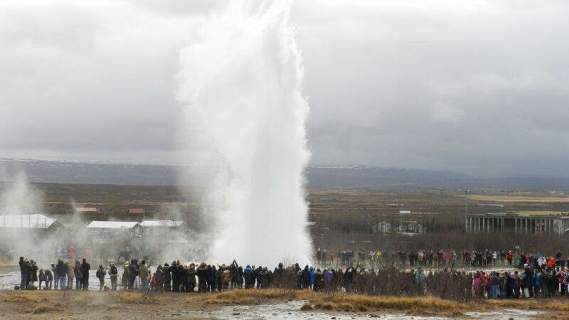 a geysir spurting water high into the air with a crowd of people gathered around