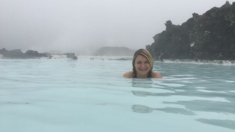 a girl sat in the blue lagoon in iceland with steam rising around her