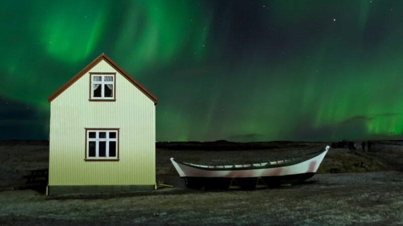 a house and boat with the northern lights glowing behind