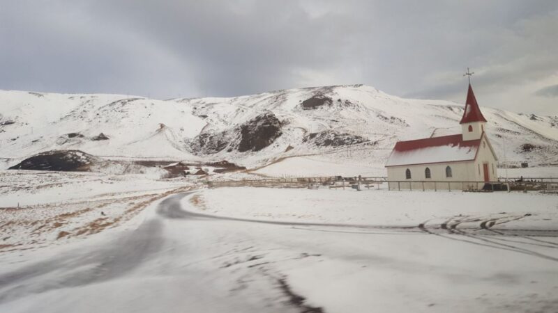 a snow covered church with a red roof and huge snowy mountains in the background